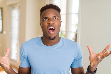 Yakışıklı afro-amerikan adam rahat t-shirt deli ve deli bağırarak giyen ve agresif ifade ve kollar kaldırdı ile bağırıyor. Hayal kırıklığı kavramı.