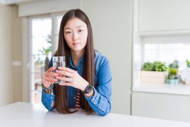 Güzel Asyalı kadın ciddi düşünme akıllı yüz üzerinde emin bir ifade ile tatlı su bir bardak içme