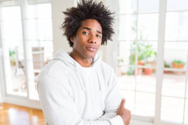 Kazak giyen Afro-Amerikan adam yüzünde ciddi bir ifade ile rahat. Çapraz kollarla basit ve doğal