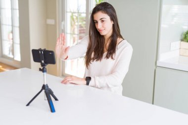 Açık el ile akıllı telefon web kamerası ile selfie video kayıt güzel genç kadın ciddi ve kendinden emin ifade, savunma jesti ile dur işareti yapıyor