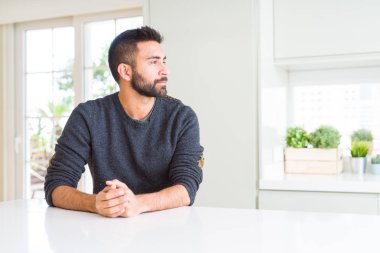 Evde yan arayan Casual kazak giyen yakışıklı İspanyol adam, güvenli bir gülümseme ile doğal yüzü ile profil poz rahatlayın.