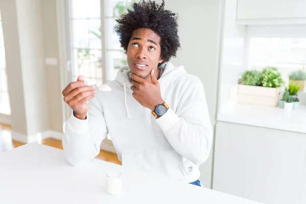 African American man eating healthy yogurt for breakfast serious face thinking about question, very confused idea