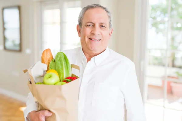 Handsome senior man holding paper bag full of fresh groceries an