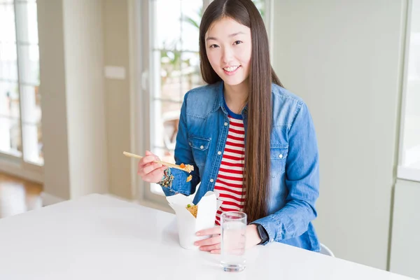 Beautiful Asian woman eating asian rice in delivery box with a happy face standing and smiling with a confident smile showing teeth