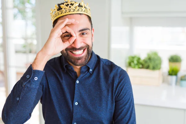 英俊的西班牙男子戴着金冠在头上作为国王做Ok手势与手微笑 眼睛透过手指与快乐的脸 — 图库照片