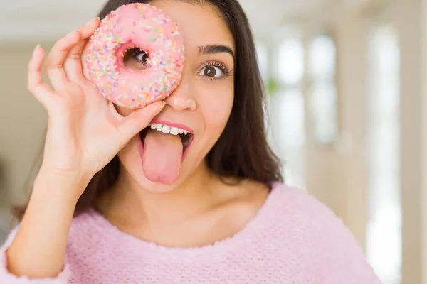 Belle jeune femme souriante regardant à travers beignet rose sur le — Photo