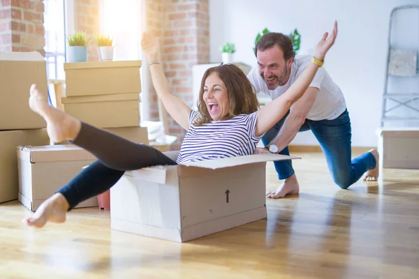 Middle age senior romantic couple having fun riding inside of cardboard, excited and smiling happy for moving to a new home