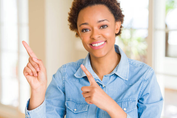 Молодая красивая африканская американка улыбается и смотрит в камеру, указывая двумя руками и пальцами в сторону.
.