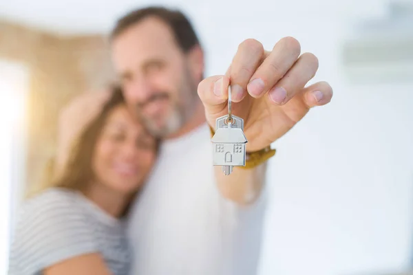 Middle age senior romantic couple holding and showing house keys, hugging and smiling happy for moving to a new home