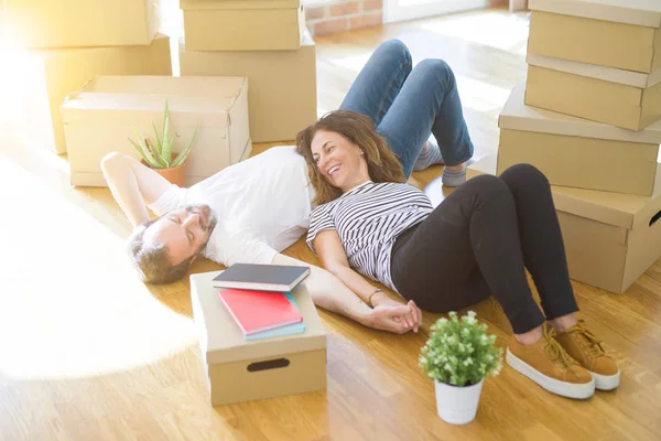 Middle age senior romantic couple lying on the floor, smiling happy for moving to a new house, relaxing and taking a break of packing boxes