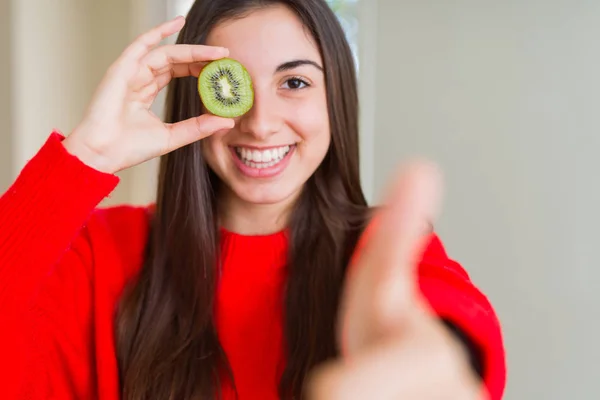美丽的年轻女子吃半新鲜的绿色奇异果快乐与大微笑做Ok标志 拇指用手指 优秀的标志 — 图库照片