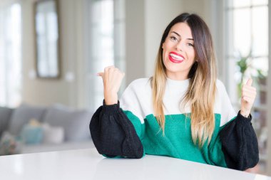 Kış kazak evde başarı işareti el ile pozitif jest yapıyor giyen genç güzel kadın başparmak gülümseyen ve mutlu. Neşeli bir ifadeyle, kazanan jest kameraya bakıyor.