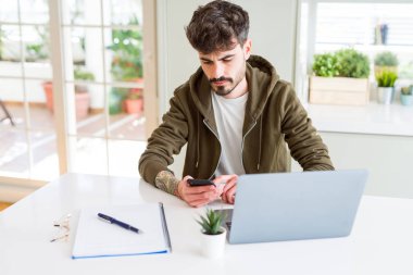 Genç bir öğrenci akıllı telefon kullanıyor ve ders çalışıyor. Akıllı bir yüz ifadesine sahip bir dizüstü bilgisayar kullanıyor. Ciddi düşünüyor.