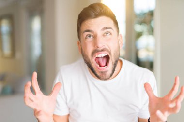 Evde çılgın ve kızgın bağırarak ve agresif ifade ve silah kaldırdı bağırmaya Casual beyaz t-shirt giyen genç yakışıklı adam. Hayal kırıklığı kavramı.