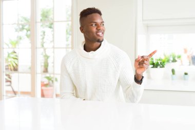 Kameraya bakarak yan el ve parmak ile işaret Afro-Amerikan yakışıklı beyaz masada yüzünde kocaman bir gülümseme ile.