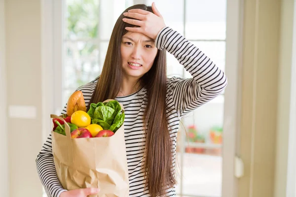 新鮮な食料品の紙袋を持つ美しいアジアの女性は 頭の上に手でストレスを感じ 恥と驚きの顔でショックを受け 怒りとイライラしました 間違いに対する恐怖と動揺 — ストック写真