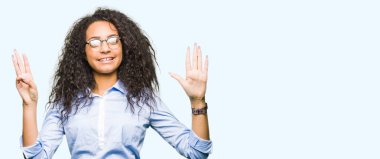 Kıvırcık saçlı Genç güzel iş kızı gösteren ve parmak sayısı sekiz ile işaret gözlük giyen emin ve mutlu gülümseyen iken.