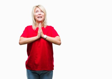Yalvarıyor ve umut ifade yüzünde çok duygusal ve endişe ile birlikte elleriyle dua izole arka plan üzerinde kırmızı t-shirt giyen genç güzel sarışın bir kadın. Bağışlanmak. Din kavramı.