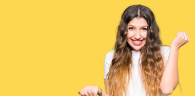 Rahat beyaz t-shirt giyen genç güzel kadın şaşırmış ve kollarını kaldırdı ve açık gözleri ile başarı için şaşırttı. Kazanan kavramı.