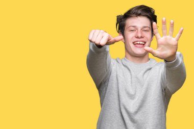 Gösterilen arka plan üzerinde sweatshirt giyen genç yakışıklı sportif adam izole ve parmakları ile işaret kendinden emin ve mutlu gülümseyerek süre 6 numara.