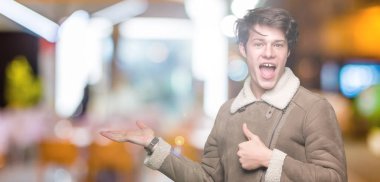 İzole arka plan gösteren palm el üzerinde kış palto giyiyor ve yukarıya, mutlu ve neşeli gülümseyen baş parmakları Tamam jest yapıyor yakışıklı delikanlı