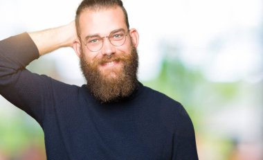 Gözlük ve balıkçı yaka kazak giyen genç sarışın adam el yukarı jest ile emin dokunmadan saç gülümsüyor, çekici poz