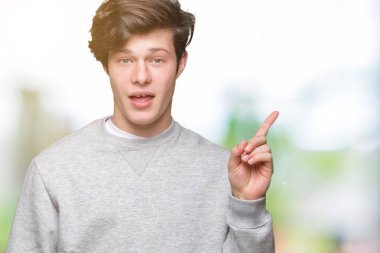 Kameraya bakarak yan el ve parmak ile işaret yüzünde kocaman bir gülümseme ile izole arka plan üzerinde sweatshirt giyen genç yakışıklı sportif adam.