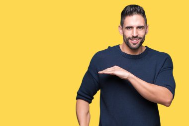 Genç yakışıklı adam ile büyük ve büyük boy işaret, ölçü birimi sembol gösteren el eller izole arka plan üzerinde kazak giyiyor. Kameraya bakarak gülümsüyordu. Ölçüm kavramı.