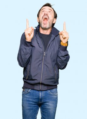 Orta yaş yakışıklı adam bir ceket hayran giyiyor ve sürpriz görünümlü ve parmaklar ve yükseltilmiş silah ile işaret.