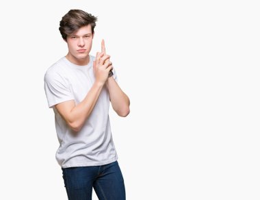 İzole arka planda rahat beyaz t-shirt giyen genç yakışıklı adam el jest ile sembolik silah tutarak, öldürme çekim silah oynarken, öfkeli yüz