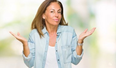 Orta yaş yetişkin kadın üzerinde rahat kot gömlek giymiş arka plan clueless ve şaşkın bir ifadeyle kollar ve eller kaldırdı izole. Şüphe kavramı.