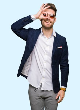 Parmakları ile mutlu yüz üzerinden seyir göz genç yakışıklı zarif adam giyen güneş gözlüğü ve moda ceket el gülümseyen, ok jest yapıyor.