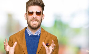 Genç yakışıklı zarif adam güneş gözlüğü giyen deli ve heyecan çığlık kapalı gözleri ile başarı için deli kutluyor. Kazanan kavramı