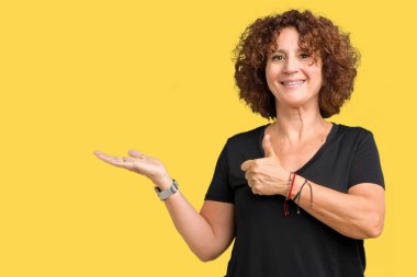 Güzel orta ager üst düzey kadın izole arka plan gösteren palm el ve yukarıya, mutlu ve neşeli gülümseyen baş parmakları Tamam jest yapıyor