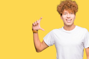 Casual beyaz gömlek gülümseyen ve süre seyir ve kamera boyutu işaret parmaklarıyla yapıyor el ile kendine güvenen el hareketi afro saçlı Genç yakışıklı adam. Ölçü kavramı.