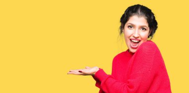 Kırmızı kazak ve topuz giyen genç güzel kadın el ve açık palmiye ile yan Işaret, reklam gülümseyen mutlu ve emin sunan