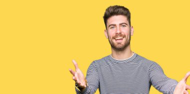 Sarılmak için Kollarını açarak gülümseyerek kameraya bakarak çizgili Süveter giyen genç yakışıklı adam. Neşeli ifade kucaklayan mutluluk.