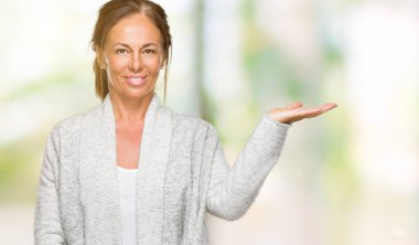 Neşeli sunulması ve kameraya bakarak avucunun ile işaret gülümseyen izole arka plan üzerinde kış kazak giyen güzel orta yaş yetişkin kadın.