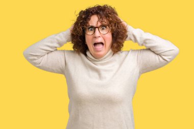 Güzel orta ager kıdemli kadın giyen balıkçı yaka kazak ve gözlük üzerinde izole arka plan çılgın ve baş elleri ile korkuyor, korku ve açık ağız ile şok şaşırttı