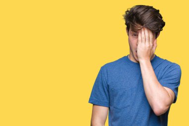 Yarım yüz, göz ve ağız el ile kapsayan yorgun esneme izole arka plan üzerinde mavi t-shirt giyen genç yakışıklı adam. Acı yüzü acıyor.