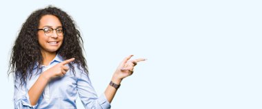 Kıvırcık saçlı Genç güzel iş kızı gözlük gülümsüyor ve iki el ve parmak tarafına işaret kamera bakarak giyiyor.