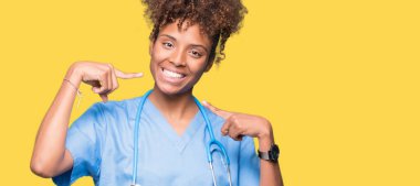 Genç Afro-Amerikan doktor kadın kendinden emin gösterilen ve işaret parmakları diş ve ağız ile gülümseyen izole arka plan yüzünden. Sağlık kavramı.