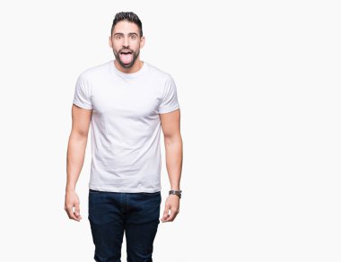 Genç adam giyiyor rahat beyaz t-shirt dilini izole arka plan üzerinde out komik ifade ile mutlu. Duygu kavramı.