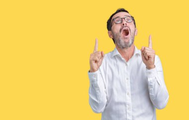 Yakışıklı orta yaş zarif üst düzey iş adamı izole arka plan üzerinde gözlük hayrete ve yukarıya bakıyor ve parmakları ile işaret ve silah kaldırdı şaşırttı.