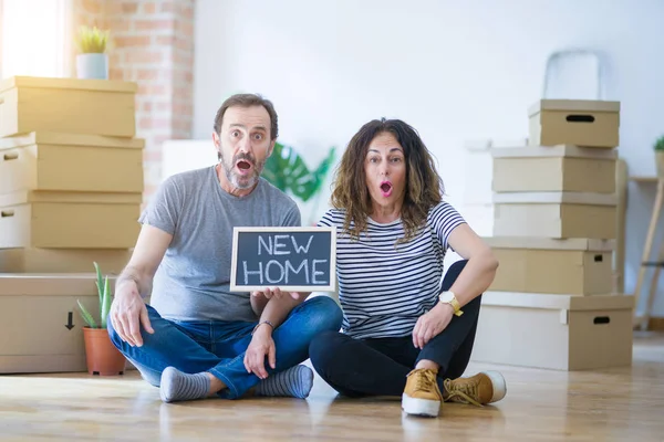 黒板を抱えて床に座る中年の高齢者夫婦は 驚きの顔でショックを受け 恐怖と恐怖表現で興奮して新しい家に移動します — ストック写真