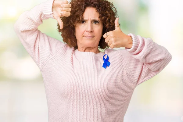 Middle ager senior woman wearing changeable blue color ribbon awareness over isolated background Doing thumbs up and down, disagreement and agreement expression. Crazy conflict