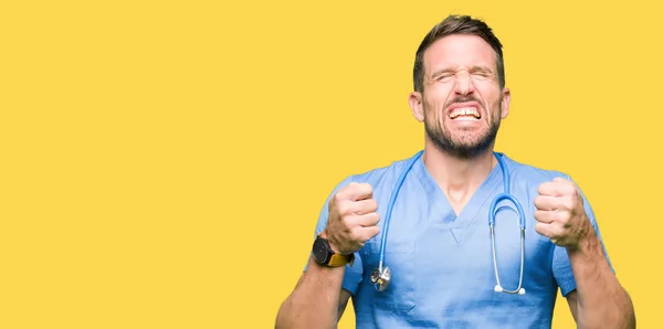英俊的医生人穿着医疗制服在孤立的背景兴奋为成功与胳膊举起庆祝胜利微笑 优胜者概念 — 图库照片