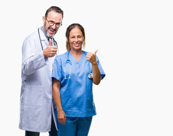 中年西班牙医生的伴侣夫妇穿着医疗制服在孤立的背景下做快乐的大拇指用手的手势 通过显示成功来批准镜头的表达 — 图库照片