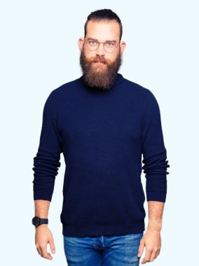 Gözlük ve balıkçı yaka kazak gevşek ciddi ifade ile yüzünde giyen genç sarışın adam. Basit ve doğal kameraya bakıyor.