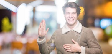 Genç yakışıklı adam giyen kış ceket izole arka plan üzerinde göğüs ve bir sadakat sözü yemin yapma avuç, el ile küfür